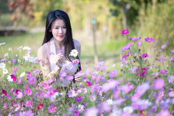 Wall Mural - Beautiful woman happy traveler walking in the flowers garden. Young woman smile and relaxing with happy  around outdoor garden. Woman's hand touching and enjoying beauty cosmos flowers.Travel concept.