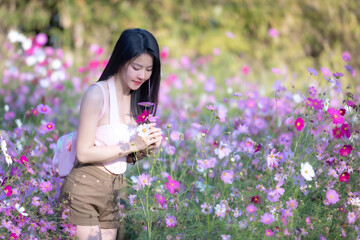 Wall Mural - Beautiful woman happy traveler walking in the flowers garden. Young woman smile and relaxing with happy  around outdoor garden. Woman's hand touching and enjoying beauty cosmos flowers.Travel concept.