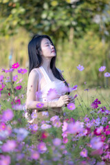 Wall Mural - Beautiful woman happy traveler walking in the flowers garden. Young woman smile and relaxing with happy  around outdoor garden. Woman's hand touching and enjoying beauty cosmos flowers.Travel concept.