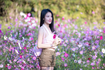Wall Mural - Beautiful woman happy traveler walking in the flowers garden. Young woman smile and relaxing with happy  around outdoor garden. Woman's hand touching and enjoying beauty cosmos flowers.Travel concept.