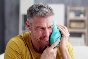 upset man touching cheek with cold water bag