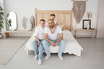 dad with two sons play in a large beautiful bedroom with large windows. happy family in a beautiful light interior.  boho style