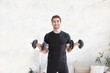 © Vitaliy - Smiling young handsome man in black sportswear doing biceps curl with dumbbells in living room at home. Healthy lifestyle and home workout concept
