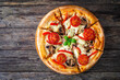 Circle vegetarian pizza with mozzarella cheese, mushrooms and tomatoes on wooden table
