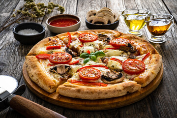 Wall Mural - Circle vegetarian pizza with mozzarella cheese, mushrooms and tomatoes on wooden table
