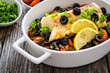 Cod in Italian style on tomatoes and black olives with baked potatoes in baking dish on wooden table

