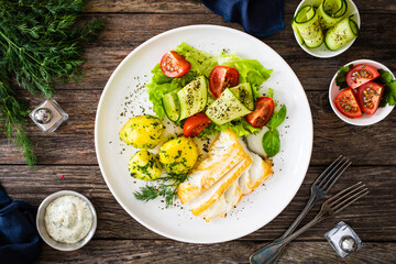 Wall Mural - Fried halibut loin with boiled potatoes and fresh vegetables on wooden table
