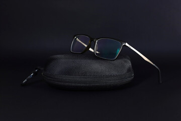 Stylish glasses for eyesight with elegant black case on black background.