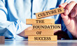 © Uuganbayar - Close up on businessman holding a wooden block with a 'Culture is the foundation of success' message