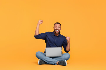Happy young man with laptop on yellow background