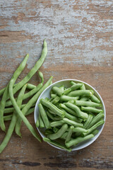 Wall Mural - fresh green beans on white bowl, aka french beans, string beans or snaps, harvested vegetable on a rustic table top, taken straight from above with copy space