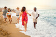 © Daniel - Young multiracial happy, smiling group of friends running along seaside during vacation travel.