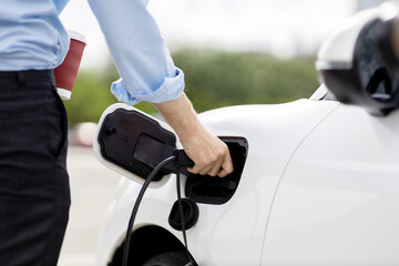 Closeup progressive man holding EV charger plug from public charging station for electric vehicle with background of residential building as concept eco-friendly sustainability energy car concept.