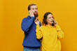 © SHOTPRIME STUDIO - Woman and man cheerful couple with phones in hand talking on cell phone crooked smile cheerful, on yellow background. The concept of real family relationships, talking on the phone, work online.