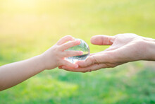 Adult Person Passes Crystal Ball To Baby Hand A Healthy Ecology To A New Generation. Healthy Ecology Of The Planet Earth. A Healthy Future For Our Generation. Green Glass Background. Save The World.