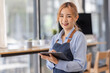 © David - Opening a small business, AHappy Asian woman in an apron standing near a bar counter coffee shop, Small business owner, restaurant, barista, cafe, Online, SME, entrepreneur, and seller concept