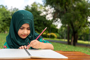 Portrait happy little asian muslim girl learn and study on table.student, asian, school, kid, child, homework.young girl writing with book and pencil making lessons in homeschool at park.Education