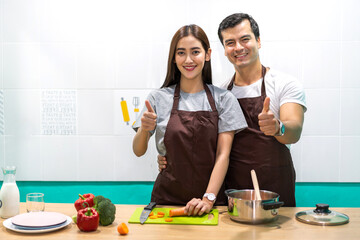 Young asian family couple having fun cooking and preparing cook vegan food healthy eat with fresh vegetable salad on counter in kitchen at home.Happy couple looking to preparing food