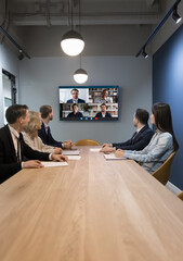 Wall Mural - team of businesspeople meeting at table in small conference room, discussing work project with remot