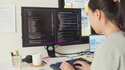 Side view of professional young Asia girl IT development programmer typing on keyboard coding programming fixing data code on computer screen and laptop on table in workroom at house office.