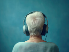 Cheerful Elderly Woman With Headphones, View From The Back, On A Blue Background. Generative Ai