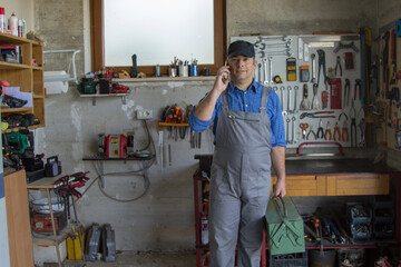 Canvas Print - Image of a handyman in his workshop talking on the phone and holding a toolbox. Answering a call for work.
