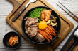 Kimchi fried rice with fried brisket and wakame seaweed and raw egg in black bowl on wooden table,(bibimbap).