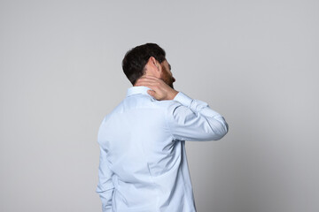 Wall Mural - Man suffering from pain in his neck on light background, back view. Arthritis symptoms