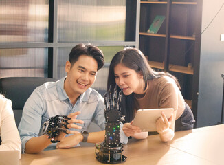 An Asian businessman controlling an artificial robotic hand. Multi-ethnic business people are examining a finger touch system in a conference room. Futuristic robot concept 