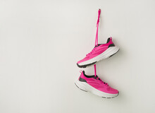 Pair Of Stylish Pink Sneakers Hanging On White Wall Background. Fashionable Stylish Sport Casual Shoes. Modern Creative Minimalistic Layout With Footwear. Mock Up For Design Advertising For Shoe Store