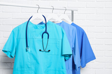 Wall Mural - Medical uniforms and stethoscope hanging on rack near white brick wall