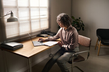 Leinwandbilder - Mature professional counselor in smart casualwear consulting patients online while sitting in front of laptop by workplace in office
