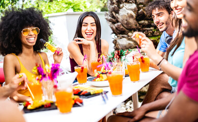 Trendy people drinking fancy cocktails at poolside garden party - Young friends having fun on luxury resort - Life style concept with men and women toasting drinks together - Bright vivid filter