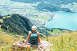 © Michael - Young woman sits on a rock next to the hiking trail and enjoys the view of lake Walensee and Walenstadt.  Schnürliweg, Walensee, St. Gallen, Switzerland, Europe.