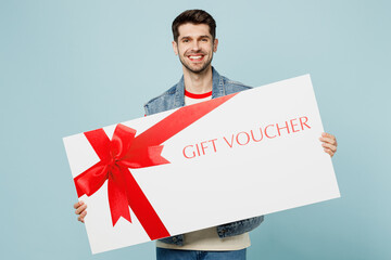 Wall Mural - Young fun man he wear denim vest red t-shirt casual clothes hold huge large gift certificate coupon voucher card for store isolated on plain pastel light blue cyan background studio. Lifestyle concept
