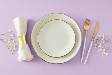 Wall Mural - Beautiful table setting concept. Top view photo of empty plate cutlery knife fork napkin with ring and gypsophila flowers on light violet background. Flat lay with empty space for message or advert