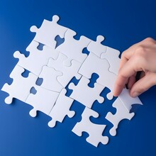 A Birds Eye View Of A Hand Moving A Large White Puzzle Piece On A Plain Royal Blue Background