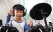 © Namphueng - Asian child boy hold drumstick to play electronic drum with headphone and happy smiling face at home. Concept of music learning, happy relaxing time, freedom, little kid musician.