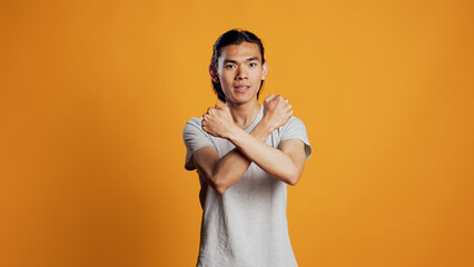 Asian person showing x shape gesture with hands, expressing refusal and disagreement. Young male model showing no symbol and rejection, refusing to listen over orange backdrop.