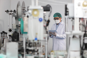 Canvas Print - Worker man in personal protective equipment or PPE inspecting quality of mask and medical face mask production line in factory, manufacturing industry and factory concept.