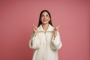 Wall Mural - Cheerful woman pointing fingers up at copy space isolated over pink background