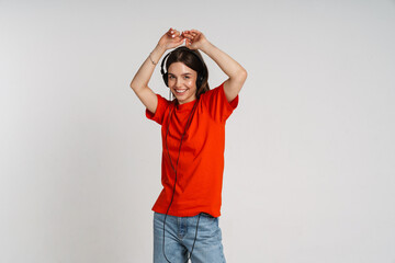 Wall Mural - Cheerful woman listening music with headphones and dancing isolated over white background