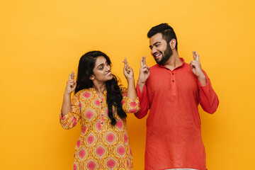 Wall Mural - Indian couple holding fingers crossed while standing isolated over yellow background