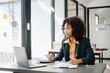 © Nuttapong punna - Confident business expert attractive smiling young woman typing laptop ang holding digital tablet on desk in office.