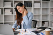 © bongkarn - Overworked asian businesswoman sits at her desk rubbing her neck, suffering from neck pain