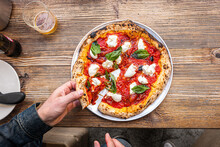 Male Hand Taking A Slice Of Pizza Freshly Baked Neapolitan Margherita Pizza On A Rustic Wooden Table In A Traditional Pizzeria.