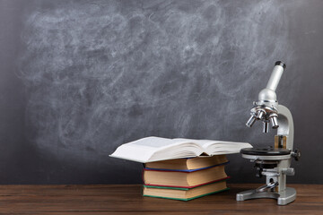 Back to school - books and microscope on the desk, Education concept. Blackboard background