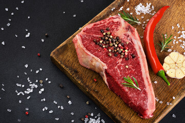 Wall Mural - Fresh raw new york steak on wooden board background with salt, pepper, rosemary, garlic and chili. Top view.