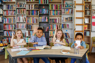 Wall Mural - Multi-ethnic pupils study and write at table in library or classroom. Back to school.