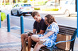© Austockphoto - Disability worker sitting at bus stop checking timetables on phone waiting for bus with teenager